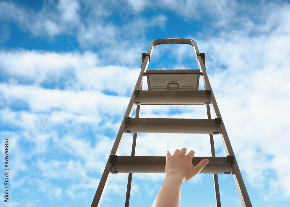 Woman climbing up stepladder against blue sky with clouds, closeup Woman climbing up stepladder against blue sky with clouds, closeup