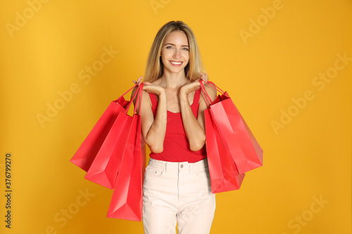 Happy young woman with shopping bags on yellow background. Black Friday Sale