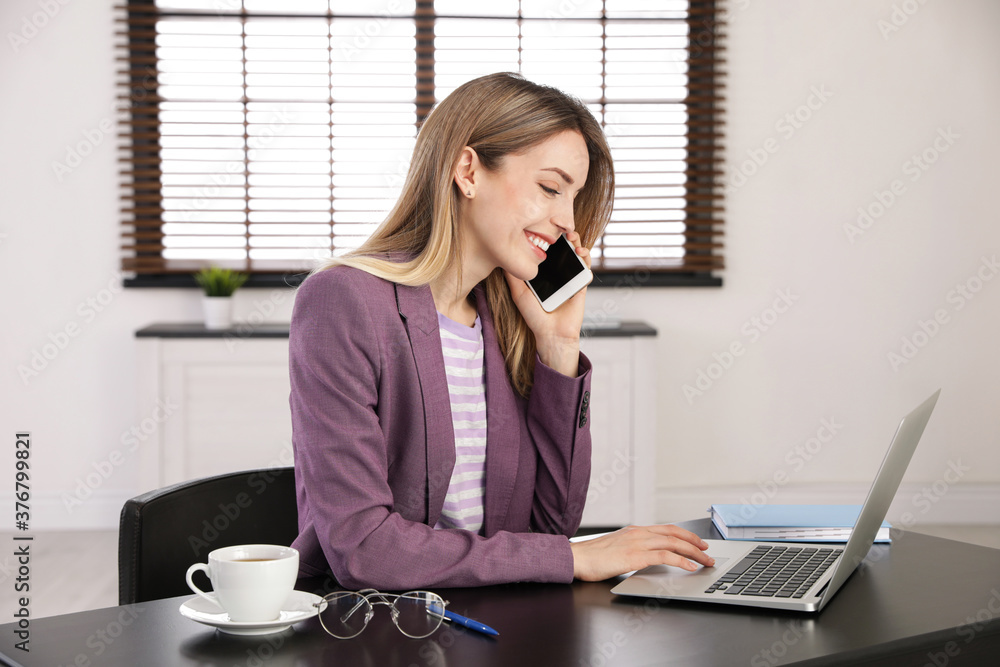 Young woman talking on phone while using laptop in office Young woman talking on phone while using laptop in office
