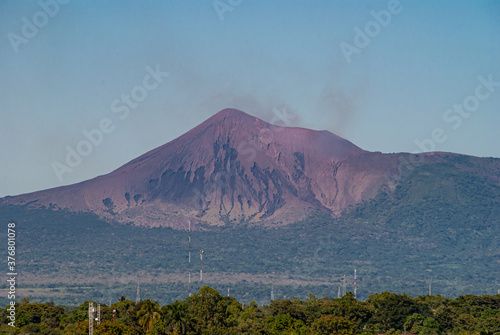 Leon, Nicaragua - November 27, 2008: Cathedral of Assumption, Asuncion. Closeup of Smoking Telica volcano in distance under blue sky and green foliage on flanks as seen from roof.
