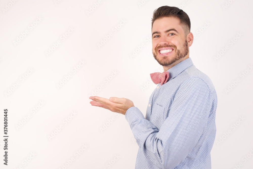 European man dressed in formal shirt and bow tie poses against white studio background pointing aside with hands open palms showing copy space, presenting advertisement smiling excited happy European man dressed in formal shirt and bow tie poses against white studio background pointing aside with hands open palms showing copy space, presenting advertisement smiling excited happy