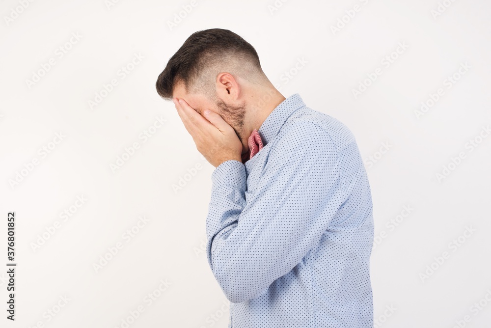 Sad European man dressed in formal shirt and bow tie poses against white background crying covering his face with her hands. Sad European man dressed in formal shirt and bow tie poses against white background crying covering his face with her hands.