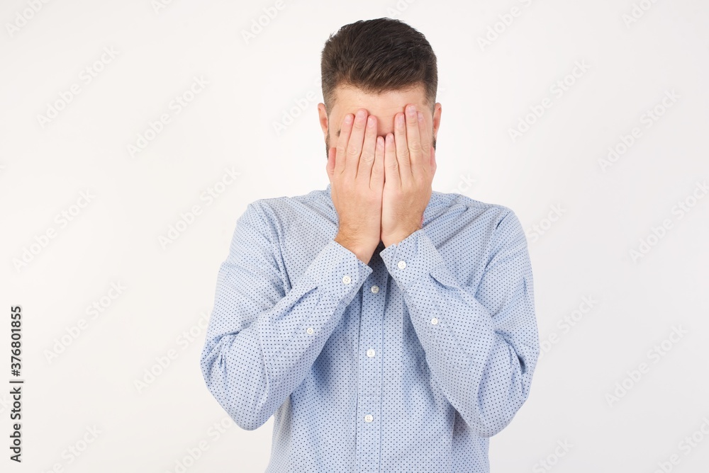 European man dressed in formal shirt and bow tie poses against white background covering his face with his hands, being devastated and crying. Sad concept European man dressed in formal shirt and bow tie poses against white background covering his face with his hands, being devastated and crying. Sad concept