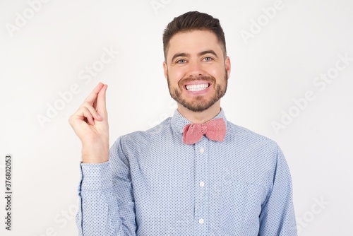 European man dressed in formal shirt and bow tie poses against white studio background pointing up with hand showing up seven fingers gesture in Chinese sign language QÄ«.