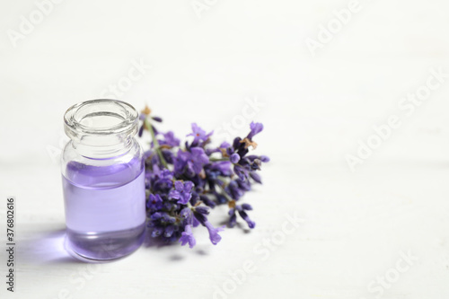 Bottle of essential oil and lavender flowers on white wooden table. Space for text