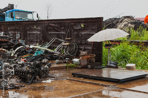 Industrial scales for weighing scrap metal under a grey umbrella on a rainy summer day.