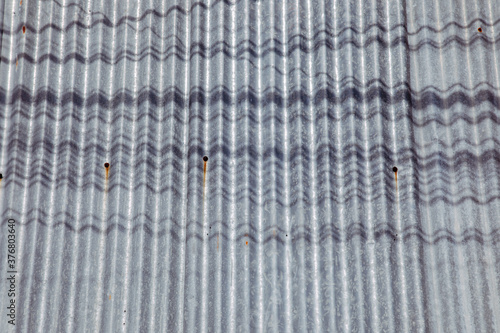 front view and close up shot of wavy roofing tiles which were made from metallic zinc shows the beautiful detail of its grunge surface texture with rusty and shadow of electricity cable line.