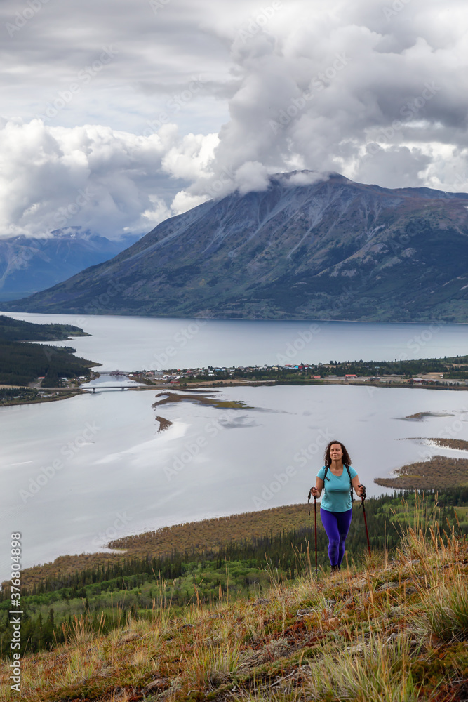 Fototapeta premium Adventurous Girl Hiking up the Nares Mountain during a cloudy and sunny evening. Taken at Carcross, near Whitehorse, Yukon, Canada.
