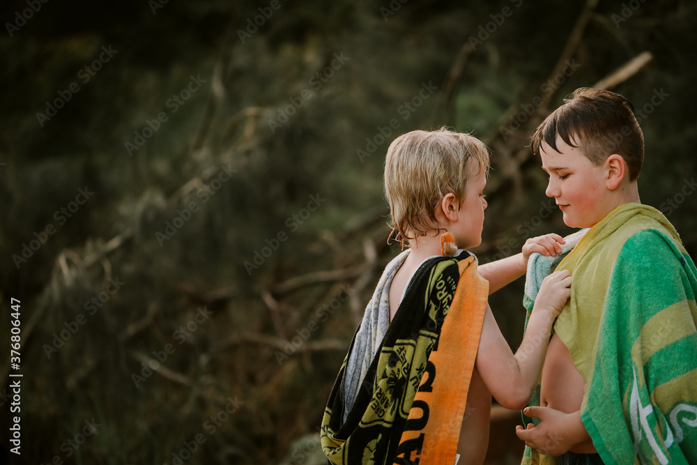 Brothers wrapped in beach towels showing affection to each other after swimming in river