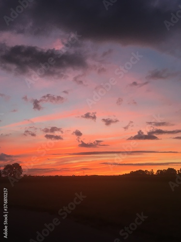 Brilliant sunset against stark country landscape that glows in yellows, oranges, peaches, light blue against pink, violet, gray and black clouds.  © Pauline
