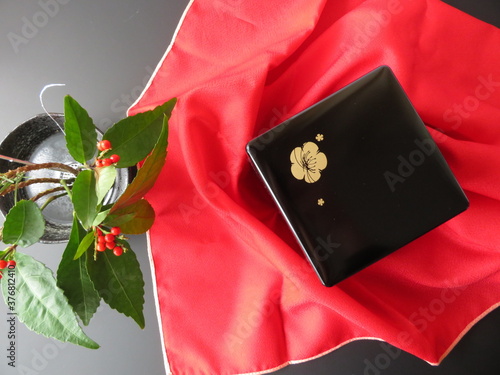 紅色の風呂敷の上に置かれた黒い重箱と南天