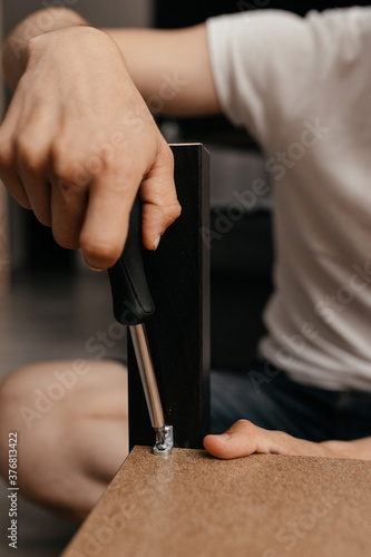 a man in casual clothes is screwing a screw into the table with a screwdriver. Close-up. Family everyday life.