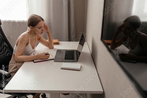 beautiful caucasian woman in casual clothes sits on a chair at a work table at home and makes notes in a notebook. work from home