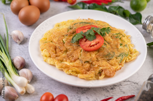 Omelet in a white plate garnished with tomatoes and coriander.