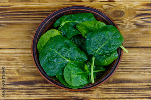 Fresh green spinach leaves in bowl on a wooden table. Top view