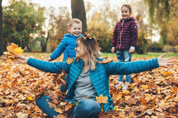 Caucasian mother with glasses is playing in leaves with her son and daughter during a walk in park