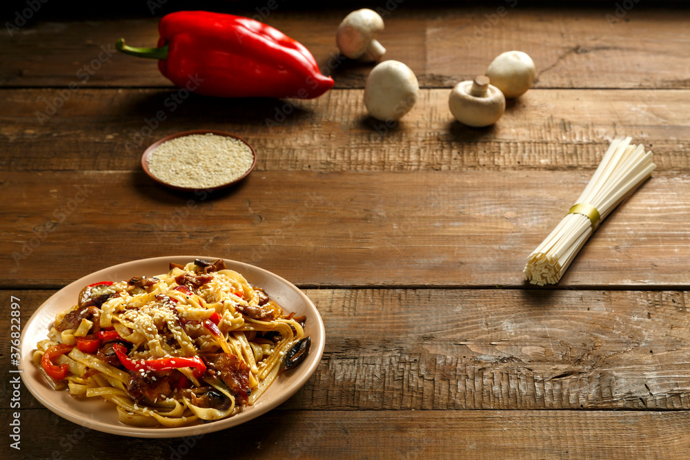Udon with vegetables and mushrooms in pad thai sauce in a beige dish near the ingredients. Udon with vegetables and mushrooms in pad thai sauce in a beige dish near the ingredients.