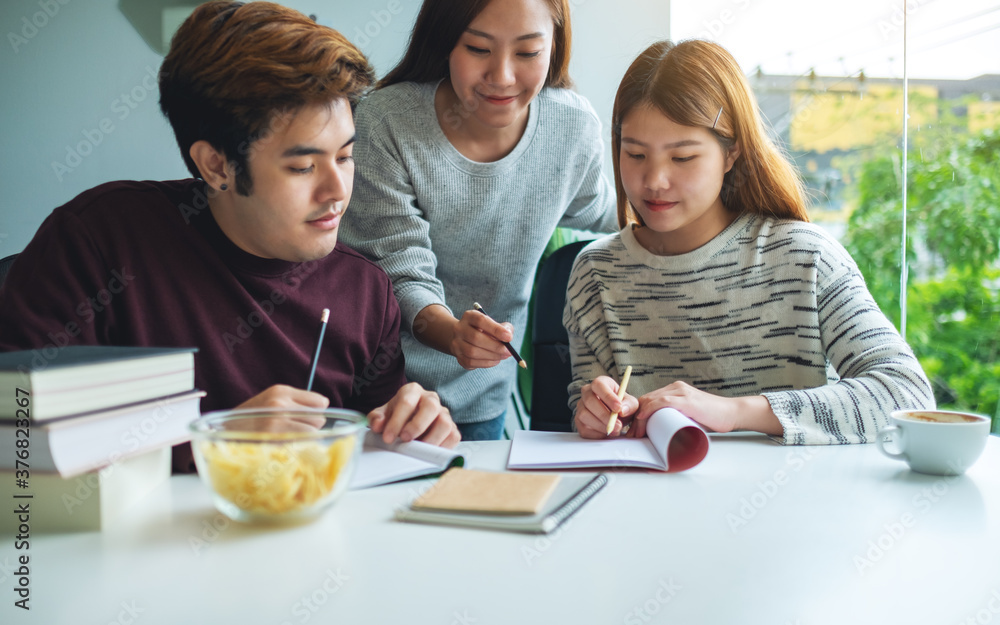 Group of young students tutoring and catching up workbook with friends Group of young students tutoring and catching up workbook with friends