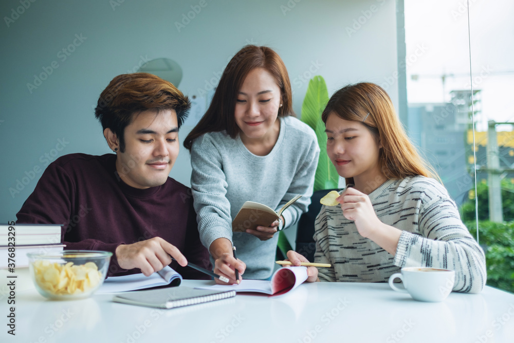 Fototapeta premium Group of young students tutoring and catching up workbook with friends