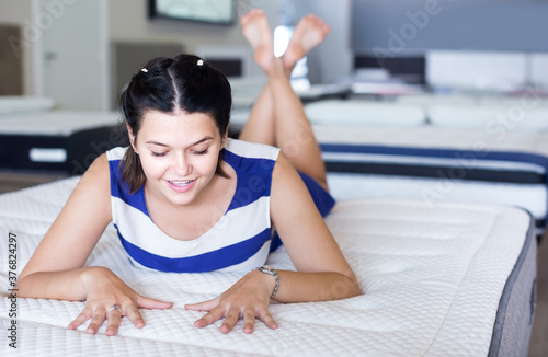 Young american woman is lying on bed and testing mattress in the store. © JackF
