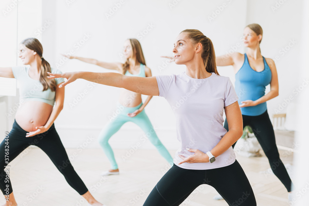Group of pregnant women in sports uniforms with coach doing gymnastic in the bright studio Group of pregnant women in sports uniforms with coach doing gymnastic in the bright studio