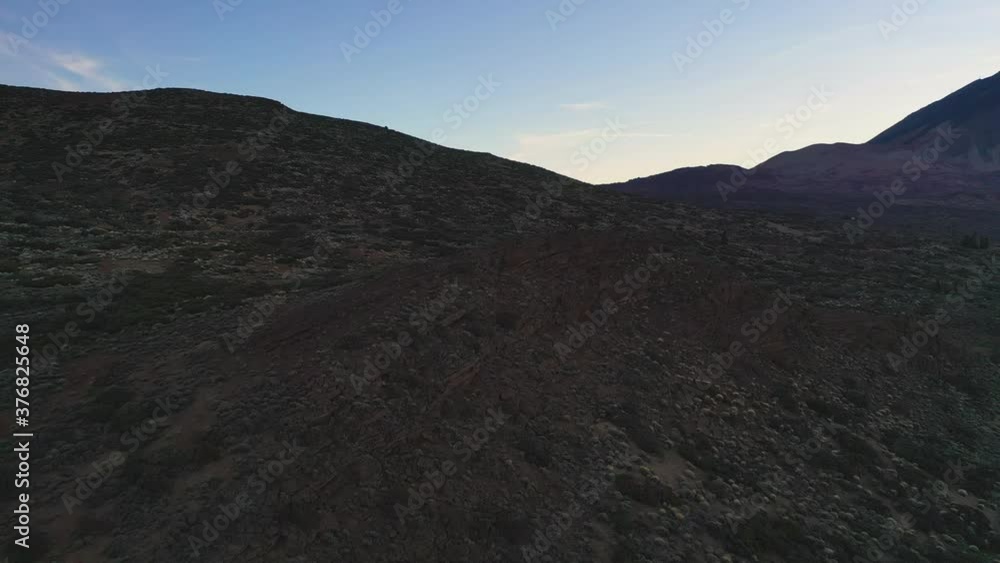 View of the cliffs and a rocky hillside below the Pico de Teide mountain on Canary Islands after sunset against a colorful evening sky. Cliffs and rocks below Pico de Teide in the evening 4K. View of the cliffs and a rocky hillside below the Pico de Teide mountain on Canary Islands after sunset against a colorful evening sky. Cliffs and rocks below Pico de Teide in the evening 4K.