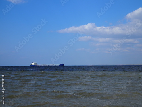 Blue shades horizon. Cargo ship against cloudy blue sky and rippled sea
