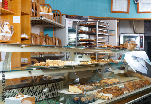 Fototapeta Interior of small bakery shop with racks and showcase full of pastries and baked goods
