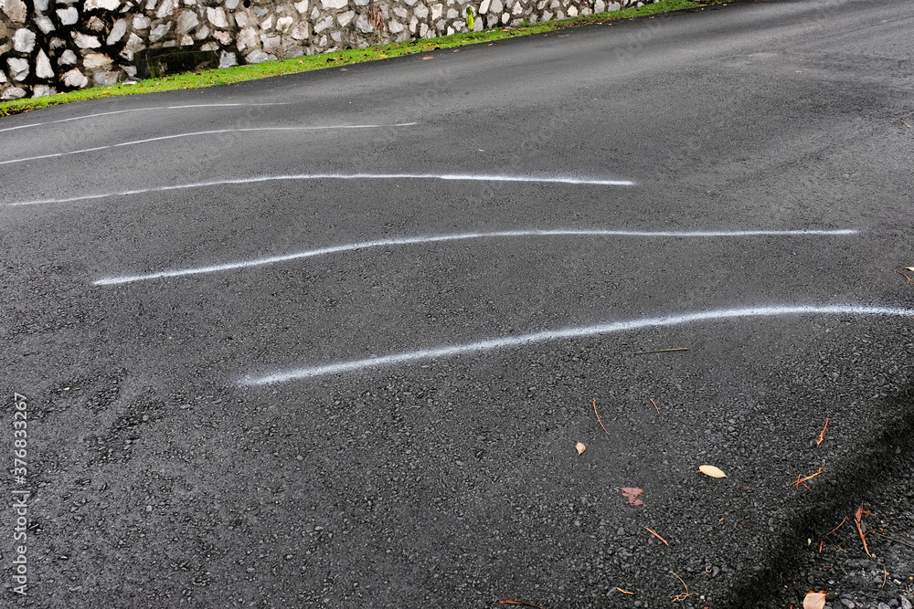 White stripes being sprayed on a speed bump after being tarred, acting as a quick and easy interim solution to warn road users. Road hump temporarily painted with white lines after a new coat of tar.