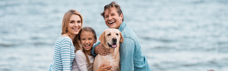 Panoramic shot of family embracing golden retriever on beach