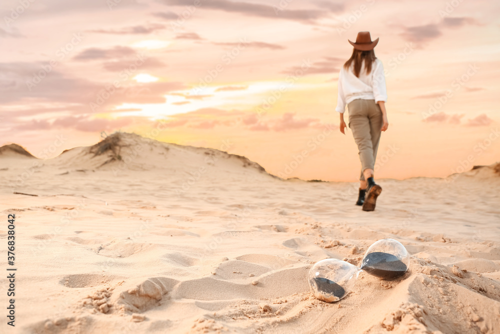 Hourglass on sand and walking woman in desert Hourglass on sand and walking woman in desert