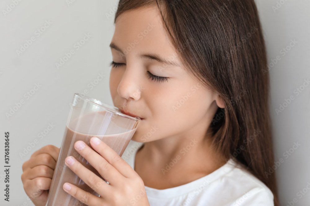 Little girl drinking tasty chocolate milk on light background Little girl drinking tasty chocolate milk on light background
