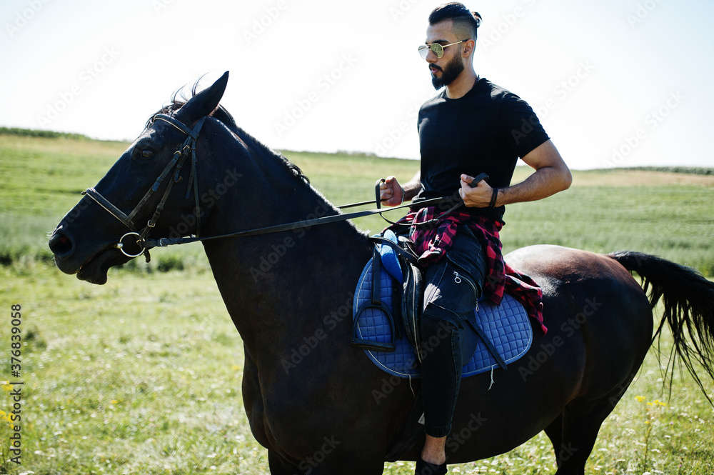 Obraz premium Arab tall beard man wear in black and sunglasses ride arabian horse.