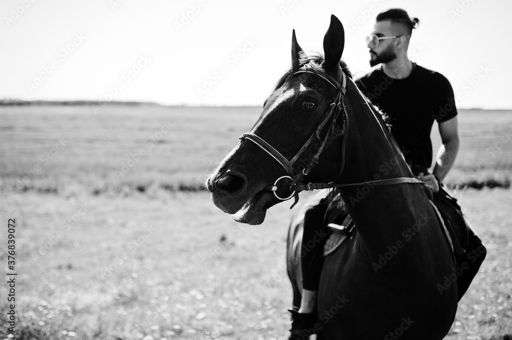 Obraz premium Arab tall beard man wear in black and sunglasses ride arabian horse.