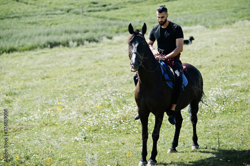 Arab tall beard man wear in black ride arabian horse.