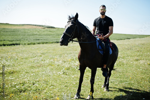 Arab tall beard man wear in black and sunglasses ride arabian horse.