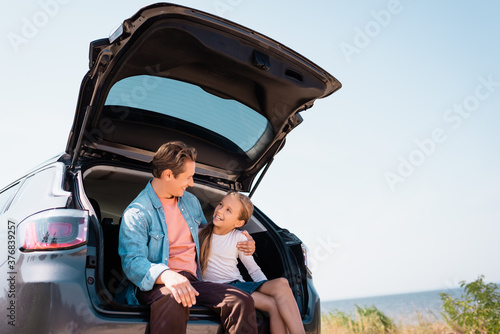 Father hugging child while sitting in trunk of auto on beach © LIGHTFIELD STUDIOS