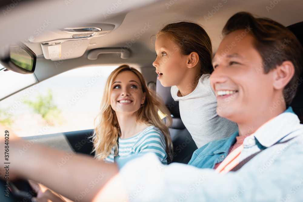 Selective focus of excited girl looking away while traveling with parents in car Selective focus of excited girl looking away while traveling with parents in car