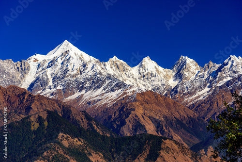 View of Snow cladded Panchchuli peaks falls in great Himalayan mountain range & alpine grass meadows enroute to Khalia Top trekk trail at small hamlet Munsiyari, Kumaon region, Uttarakhand, India.