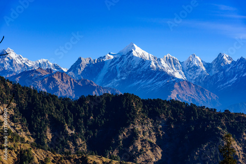 View of Snow cladded Panchchuli peaks falls in great Himalayan mountain range & alpine grass meadows enroute to Khalia Top trekk trail at small hamlet Munsiyari, Kumaon region, Uttarakhand, India.