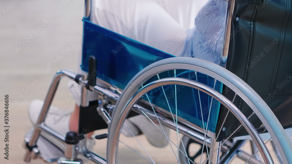 Fototapeta premium Disabled old woman holding hands on chair wheell in hospital hallway. Disabled disability handicapped impairment disease treatment and patient paralysis