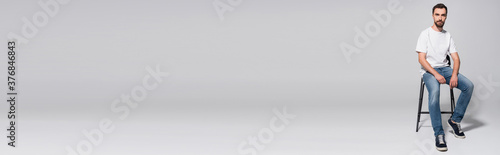 Foto horizontal image of young man in white t-shirt and jeans sitting on chair and lo
