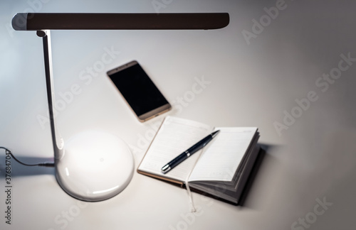 Obraz na płótnie A smartphone and open diary with a pen on the table under the desktop LED lamp