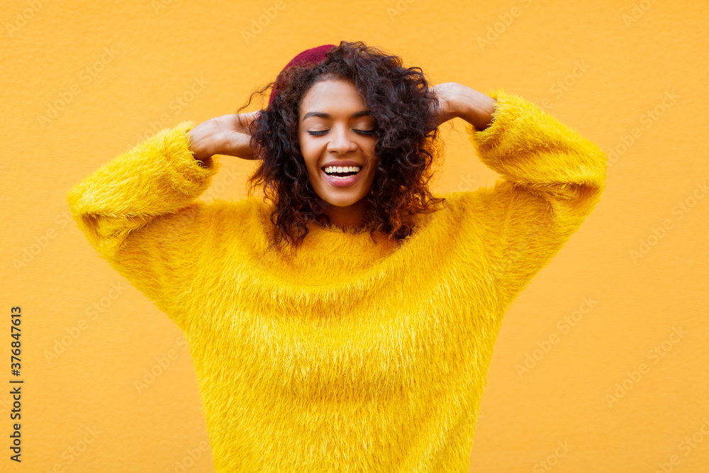 Gorgeous black smiling woman with clothes eyes playing with her curly hair on yellow background in cute fluffy sweater and Burgundy beret. Gorgeous black smiling woman with clothes eyes playing with her curly hair on yellow background in cute fluffy sweater and Burgundy beret.