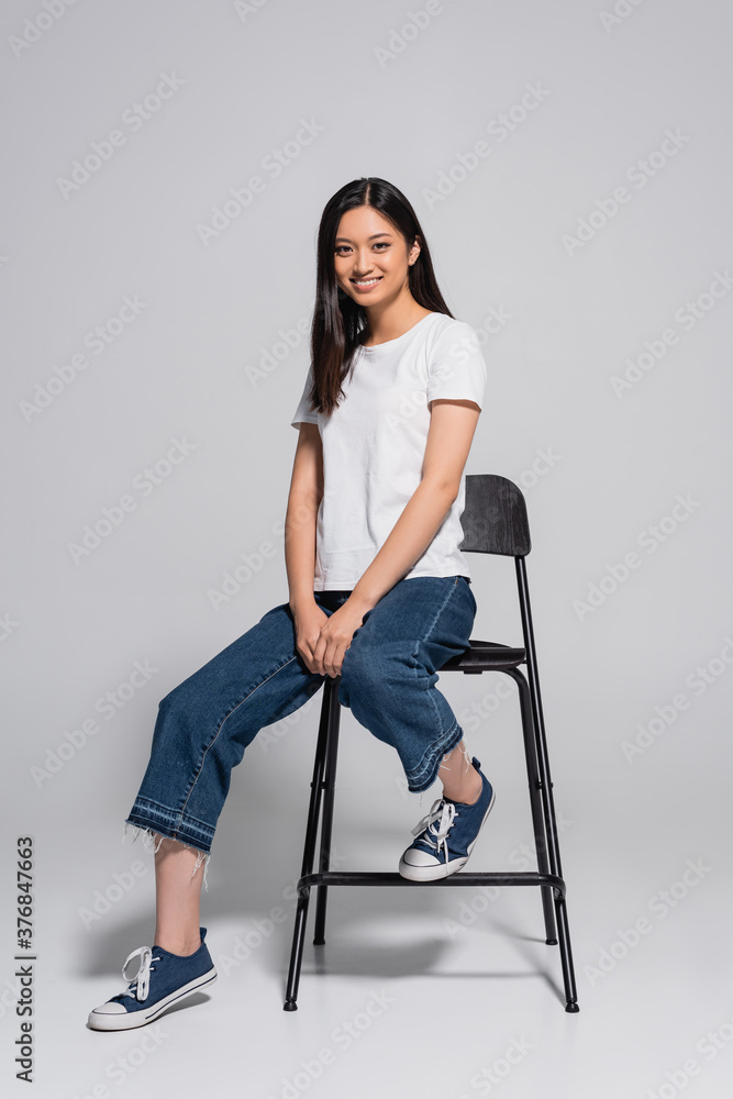 Φωτογραφία brunette asian woman in jeans, gumshoes and white t-shirt sitting on chair and l