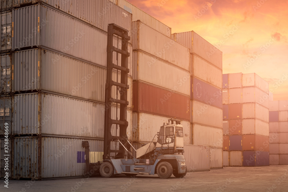 Forklift truck lifting cargo container in shipping yard or dock yard against sunrise sky with cargo container stack in background for transportation import,export and logistic industrial concept Forklift truck lifting cargo container in shipping yard or dock yard against sunrise sky with cargo container stack in background for transportation import,export and logistic industrial concept