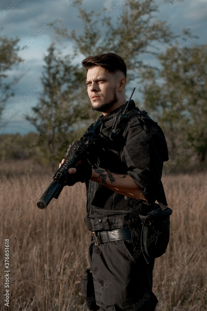 Fototapeta premium Young soldier in black uniform with an assault rifle.