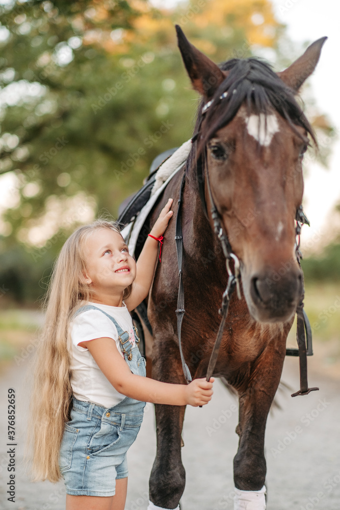 Obraz premium Friendship of a child with a horse. A little girl is affectionately stroking her horse. Walking girls with a horse in the park in autumn.