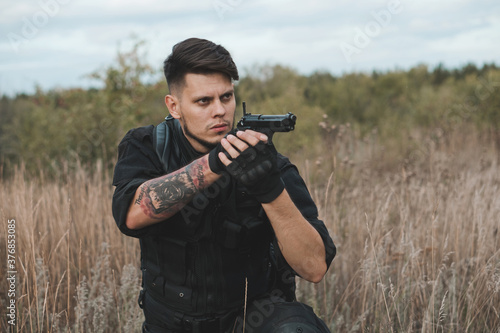 Young soldier in black uniform sitting and aiming a pistol.