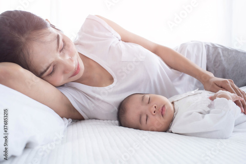 Loving mom carying of her newborn baby at home. Bright portrait of happy mum holding sleeping infant child on hands. Mother hugging her little. Mother and her baby son, sleeping on a big bed.